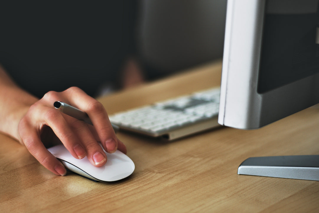 Hand using a computer mouse at a desk with a modern keyboard and monitor