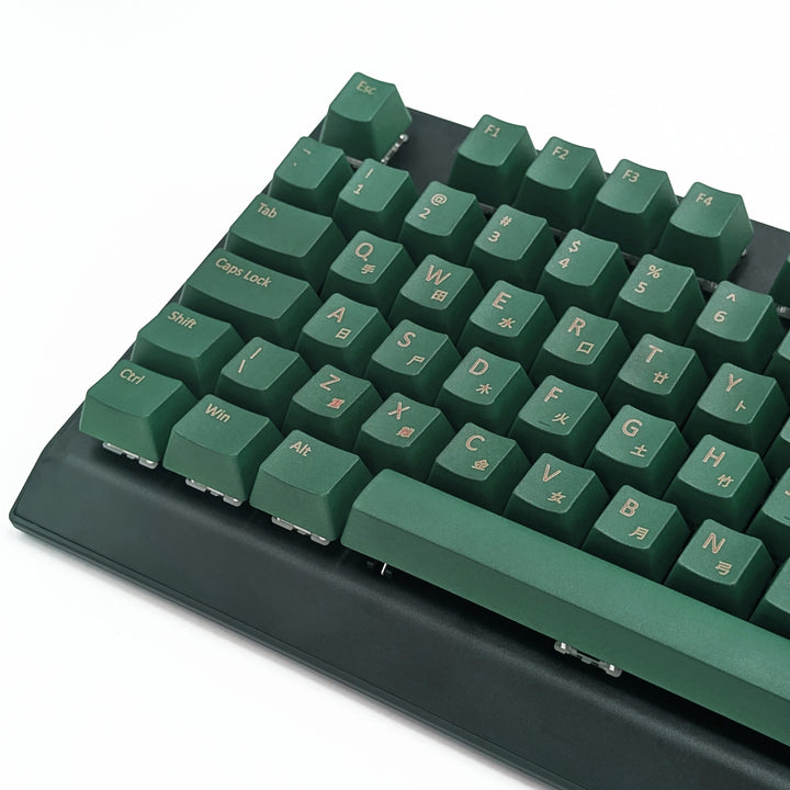 Close-up of green QWERTY PBT keycaps with gold legends, non-backlit OEM profile keys with a matte finish on a mechanical keyboard.