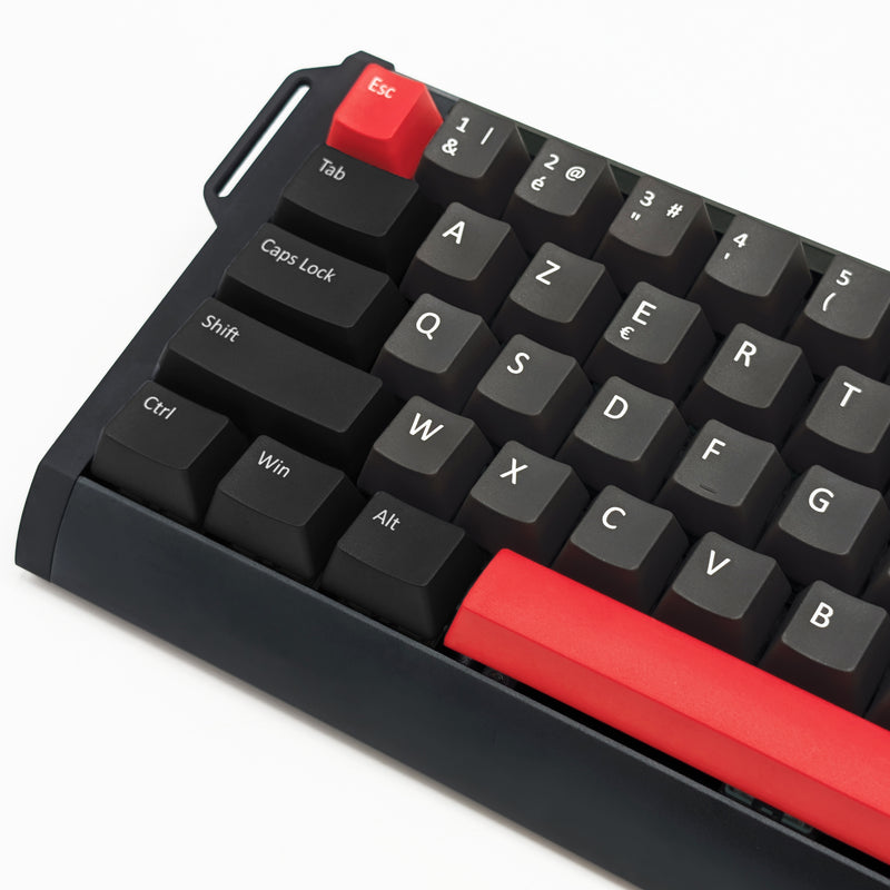 Close-up of a compact mechanical keyboard with black keycaps and a bright red escape key and large red backspace key, shown on a white background.