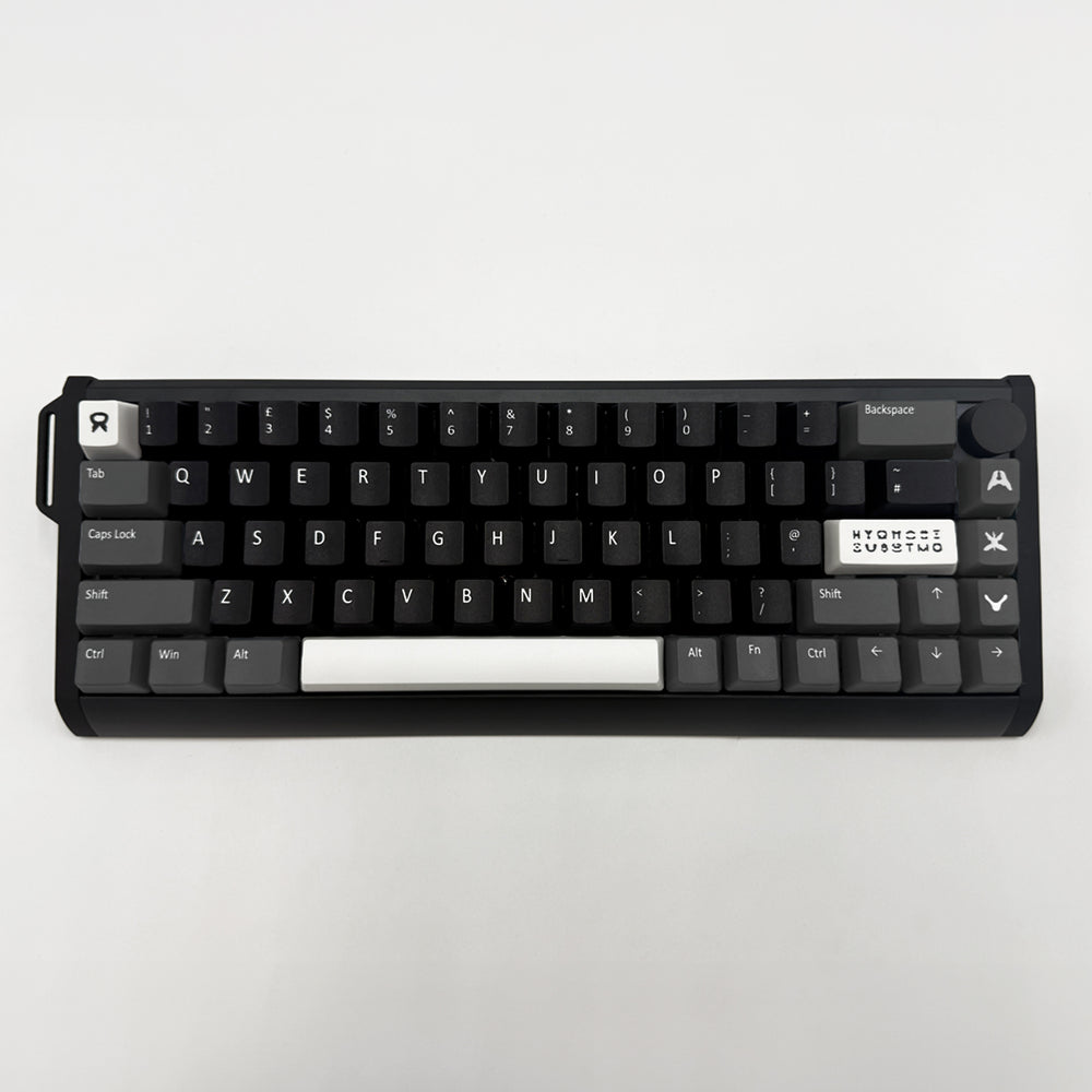 A compact mechanical keyboard with black keycaps and a white spacebar, photographed from directly above on a light gray background.