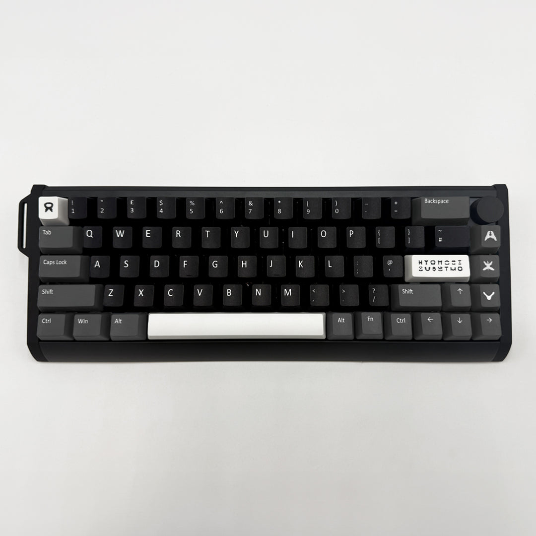 A compact mechanical keyboard with black keycaps and a white spacebar, photographed from directly above on a light gray background.