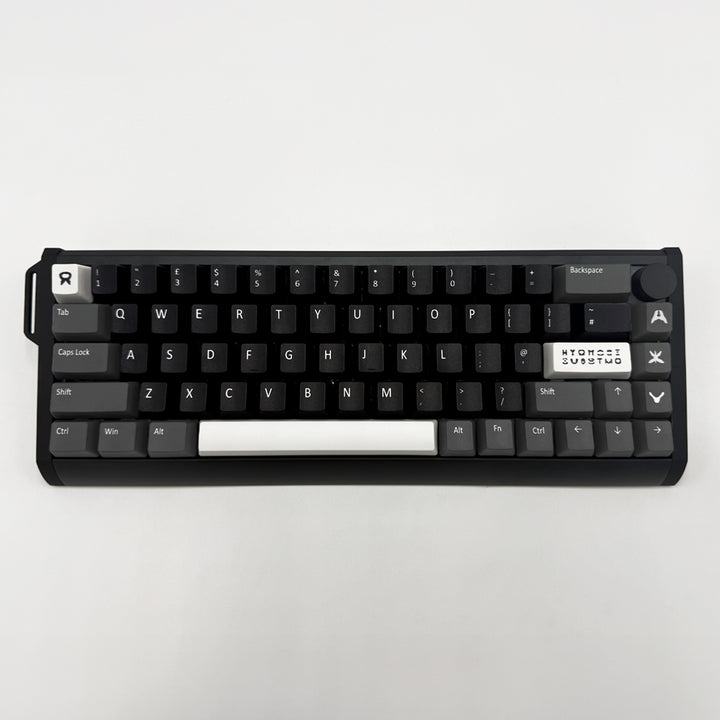 A compact mechanical keyboard with black keycaps and a white spacebar, photographed from directly above on a light gray background.