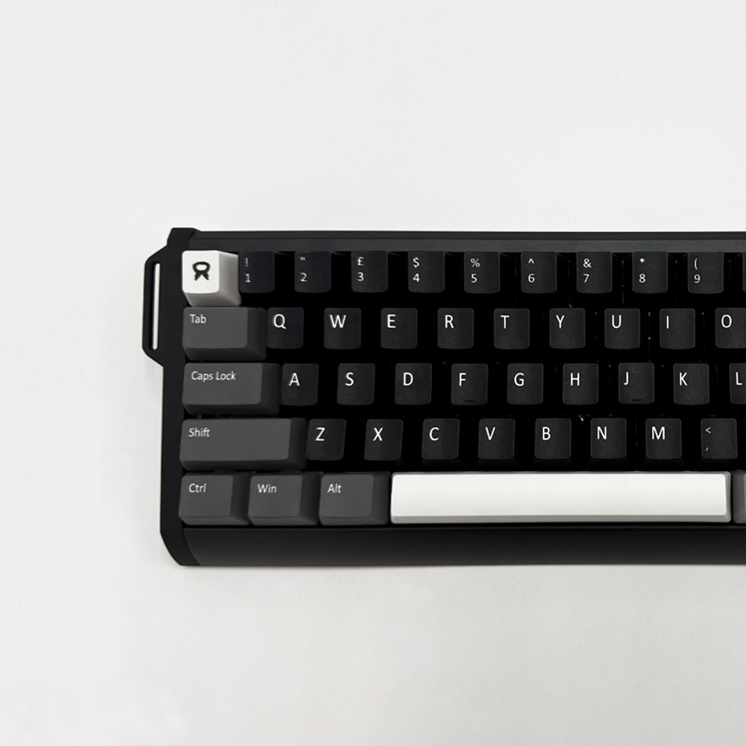 A close-up of a mechanical keyboard with a black frame and black keycaps, featuring white keycaps for the Tab, Caps Lock, Shift, Ctrl, Win, and Alt keys, and a white R keycap with a stylized logo. The keyboard is photographed from a top-down angle on a clean, light off-white background.