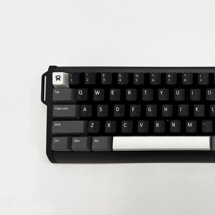 A close-up of a mechanical keyboard with a black frame and black keycaps, featuring white keycaps for the Tab, Caps Lock, Shift, Ctrl, Win, and Alt keys, and a white R keycap with a stylized logo. The keyboard is photographed from a top-down angle on a clean, light off-white background.