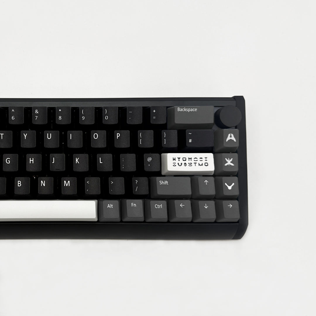 A close-up of a black mechanical keyboard showing the top row keys, including a white custom keycap with the text &