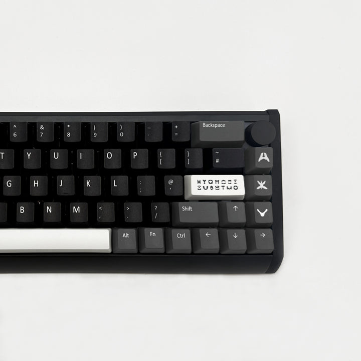 A close-up of a black mechanical keyboard showing the top row keys, including a white custom keycap with the text &